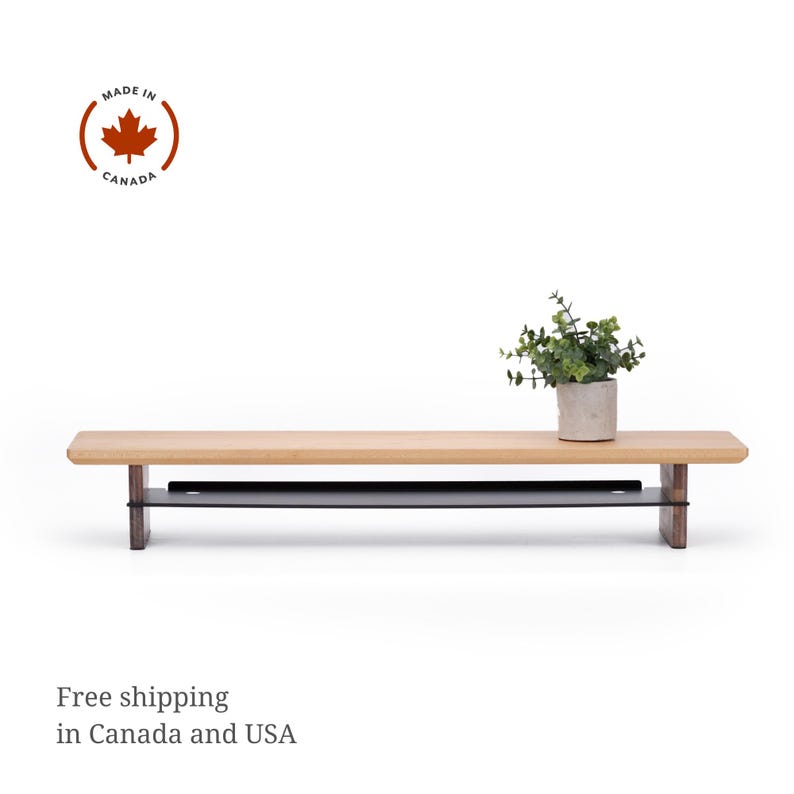 May include: A light wood shelf with a black metal shelf underneath. The shelf is sitting on a white surface. A small potted plant is sitting on the top shelf.