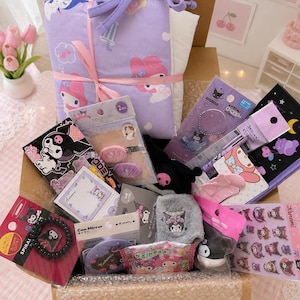 Pode incluir: Uma caixa de papelão cheia de diversos produtos dos personagens Sanrio, incluindo um item de tecido lavanda com estampa da My Melody, acessórios de cabelo da Kuromi, um elástico de cabelo em espiral, um pequeno espelho, adesivos e papelaria.