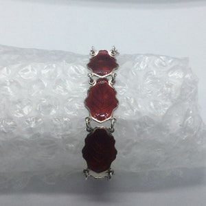 Puede incluir: Un brazalete de plata con tres hojas de esmalte rojo. Las hojas están conectadas por eslabones de plata.