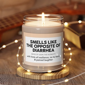 May include: A brown glass candle with a white label that reads "Smells like the opposite of diarrhea. Made of 100% the audacity with hints of resilience, no tp tears, & pained laughter."