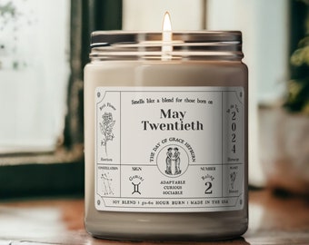 May include: A beige candle with a white label that reads "Smells like a blend for those born on May Twentieth." The label also includes the text "The Day of Grace Hepburn", "Gemini", "Adaptable Curious Sociable", "Number Ruling 2", "Soy Blend 50-60 Hour Burn | Made in the USA".