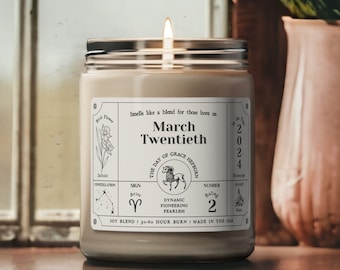 May include: A beige candle with a black lid and a white label. The label has the text "March Twentieth" and astrological symbols. The candle is lit and the flame is visible.