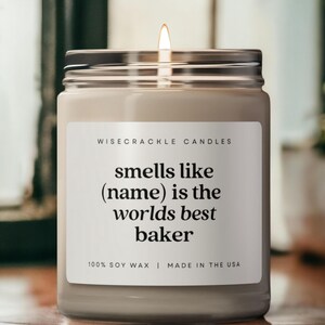 May include: A white candle with a black label that reads "WISECRACKLE CANDLES smells like (name) is the worlds best baker 100% SOY WAX | MADE IN THE USA".