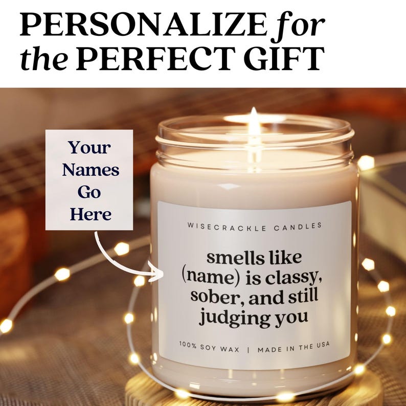 May include: A white candle with a black label that reads "smells like (name) is classy, sober, and still judging you". The label also says "Wisecrackle Candles" and "100% Soy Wax | Made in the USA".