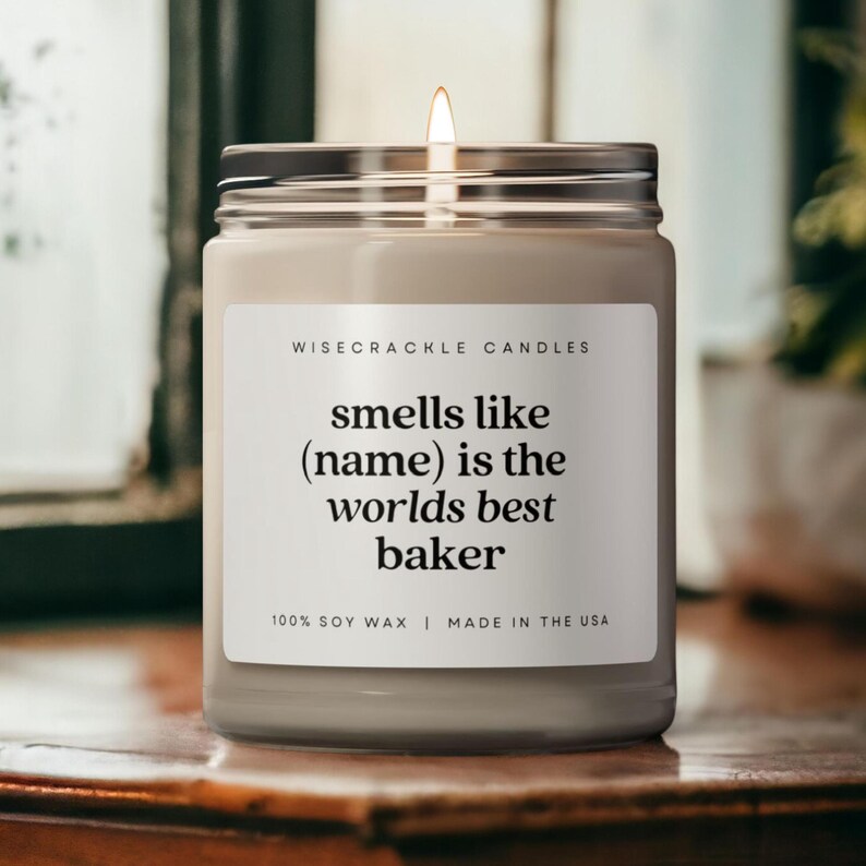 May include: A white candle with a black label that reads "WISECRACKLE CANDLES smells like (name) is the worlds best baker 100% SOY WAX | MADE IN THE USA".