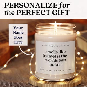 May include: A white candle with a label that reads "WISECRACKLE CANDLES" and "smells like (name) is the worlds best baker". The candle is on a wooden base with a string of lights around it.
