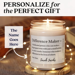K&ouml;nnte beinhalten: Eine personalisierte Kerze mit dem Text "Difference Maker (n)" und einer Definition des Wortes. Die Kerze steht auf einem Holzsockel und ist von Lichterketten umgeben. Der Text "The Name Goes Here" ist auf dem Bild zu sehen.