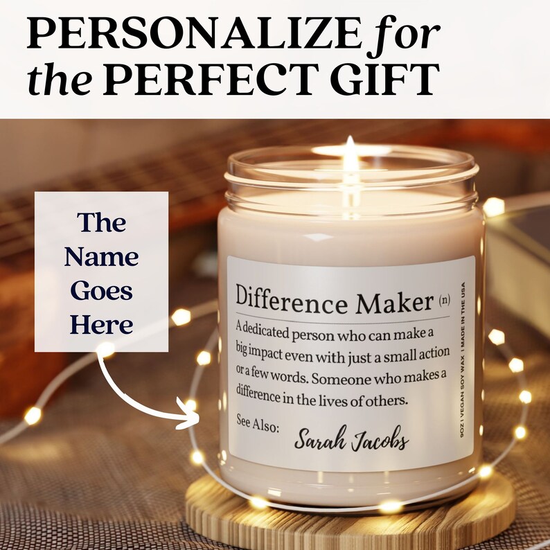 K&ouml;nnte beinhalten: Eine personalisierte Kerze mit dem Text "Difference Maker (n)" und einer Definition des Wortes. Die Kerze steht auf einem Holzsockel und ist von Lichterketten umgeben. Der Text "The Name Goes Here" ist auf dem Bild zu sehen.