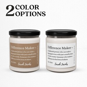 K&ouml;nnte beinhalten: Zwei wei&szlig;e Kerzenbeh&auml;lter mit schwarzen Deckeln. Die Vorderseite jedes Beh&auml;lters hat ein braunes Etikett mit dem Text "Difference Maker (n)" und einer Definition des Wortes. Der Text auf dem Etikett enth&auml;lt auch "Siehe auch: Sarah Jacobs".