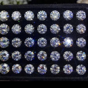 May include: A black velvet box containing 48 round, clear, faceted gemstones. The gemstones are arranged in a grid pattern.