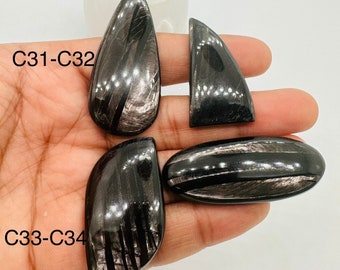 May include: Four black obsidian cabochons with silver streaks. The cabochons are labeled C31-C32 and C33-C34.