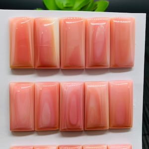 May include: A collection of fifteen rectangular, polished gemstones in shades of pink and white, arranged in three rows. Each stone measures approximately 0.47 x 0.94 inches. The stones have a marbled appearance, with swirling patterns.