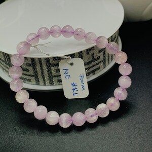 Könnte beinhalten: Ein hellviolettes Edelstein-Armband mit einem weißen Etikett, auf dem "7mm NE #K1" steht.