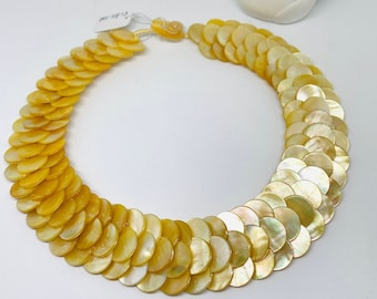 May include: A yellow and white shell necklace with a layered design. The necklace is made of many small, round shells that are arranged in a cascading pattern.