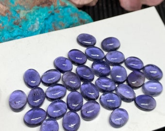 May include: A collection of 25 oval-shaped, purple gemstones. The stones are smooth and polished, with a slight shimmer.