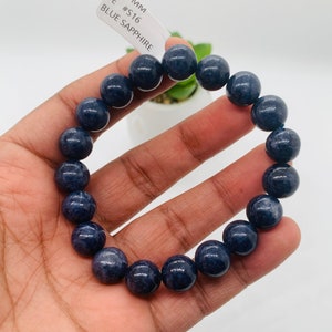 May include: A dark blue gemstone bracelet with 10.5 mm beads. The tag reads "10.5 MM TE #S16 BLUE SAPPHIRE".