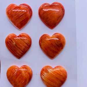 May include: Six heart-shaped decorative objects in shades of orange and red. Each heart has a glossy finish and visible grain patterns. The objects are approximately 25mm in size. The image also includes the text "6pcs".