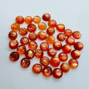 May include: A collection of 25 round, orange and gold sunstone cabochons. The stones are smooth and have a shimmery, iridescent finish.