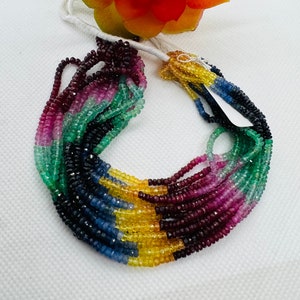 May include: A multi-strand necklace made of faceted gemstone beads. The necklace features a rainbow of colors, including red, pink, green, blue, and yellow. The beads are strung on a white cord.