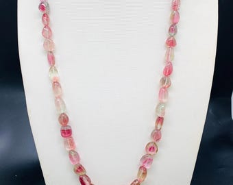 Könnte beinhalten: Eine Halskette aus rosa und klaren, ovalen Perlen. Die Perlen sind aufgereiht und bilden ein langes, elegantes Schmuckstück. Die Halskette wird auf einer weißen Schaufensterpuppe präsentiert.