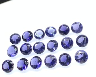 May include: A collection of 18 round, purple gemstones. The gemstones are arranged in a staggered pattern on a white surface.