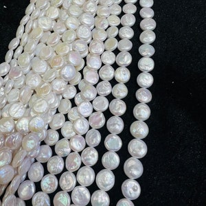 May include: Strands of lustrous, white, coin-shaped pearls. The pearls have a smooth, iridescent surface, reflecting light with a subtle sheen. The pearls are strung together, creating a flowing, elegant appearance. The background is a dark, solid color.