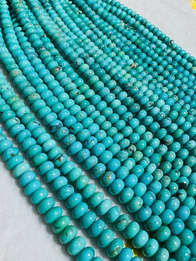 May include: A strand of turquoise beads, each bead is a light blue color with dark blue and brown veins. The beads are round and smooth, and they are strung together on a clear thread.