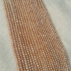 Könnte beinhalten: Eine Strähne aus vielen kleinen, hellrosa Perlen. Die Perlen sind gleichmäßig in Größe und Form und auf einem durchsichtigen Faden aufgereiht.