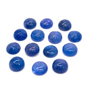 May include: A collection of fourteen smooth, round, blue glass stones. Each stone has a polished, glossy surface and a slightly irregular shape. The stones are scattered on a white background, creating a simple, clean aesthetic.