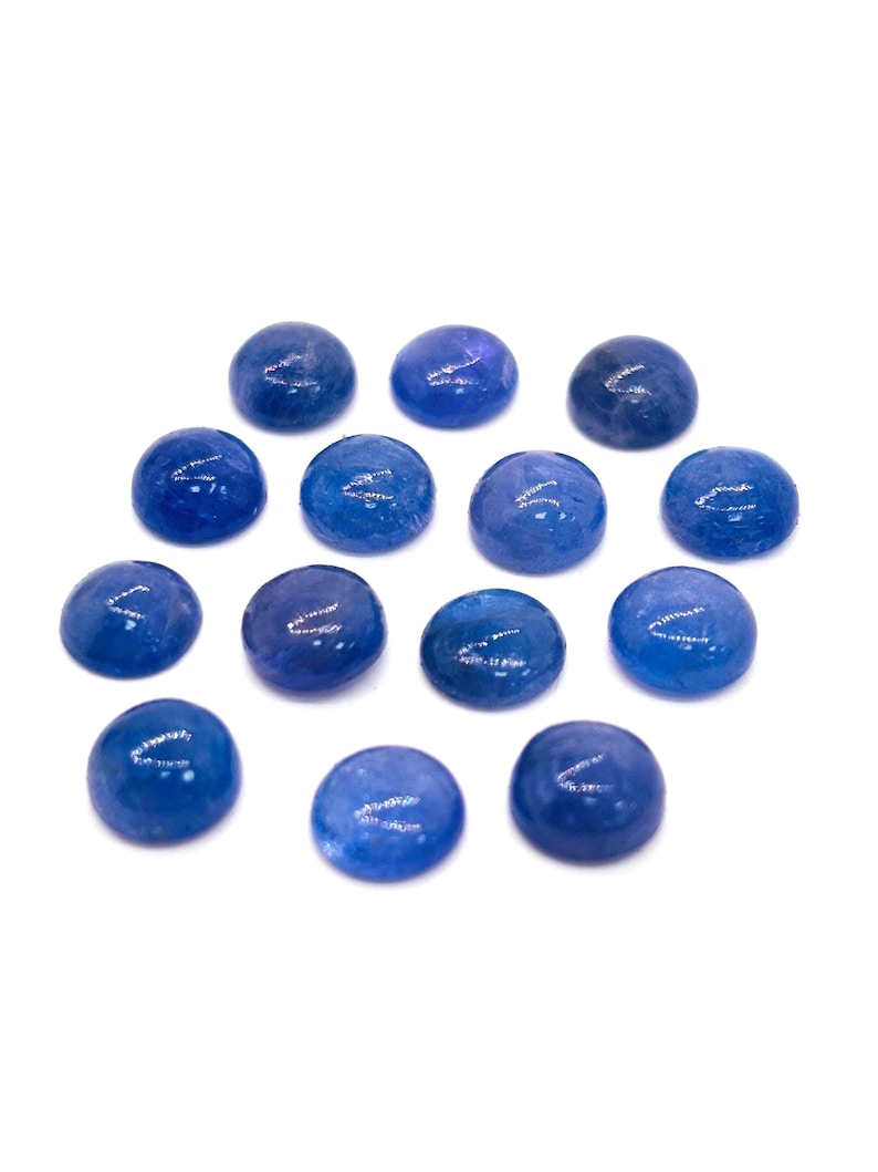 May include: A collection of fourteen smooth, round, blue glass stones. Each stone has a polished, glossy surface and a slightly irregular shape. The stones are scattered on a white background, creating a simple, clean aesthetic.