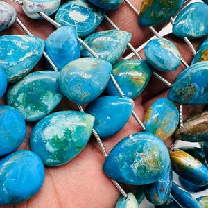 May include: A strand of turquoise blue gemstone beads with a teardrop shape. The beads have a mottled pattern of white and green.