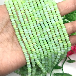 May include: A strand of light green opal beads, each bead is faceted and has a slightly irregular shape. The beads are strung on a clear thread and are approximately 3mm in diameter.