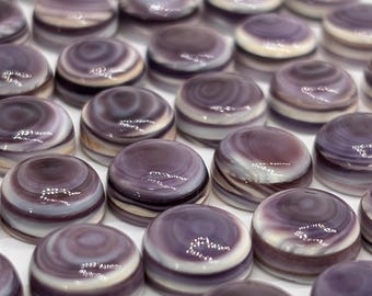 May include: A collection of small, round, purple and white swirled glass cabochons. The cabochons have a glossy finish and are arranged closely together on a white surface. The color palette includes shades of purple, lavender, and white.