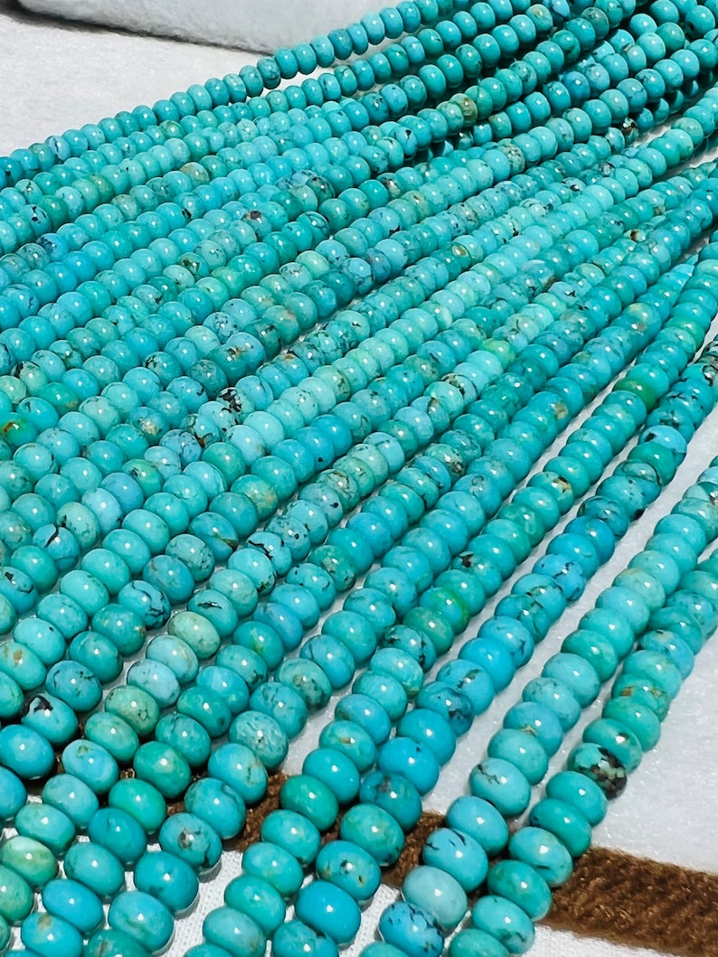 May include: A strand of turquoise beads, each bead is a light blue color with dark blue and brown marbling. The beads are round and smooth.