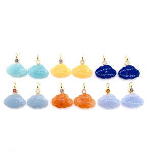 May include: A collection of cloud-shaped pendants in various colors, including blue, yellow, and orange. Each pendant has a gold-colored loop and a small gemstone accent. The pendants are displayed against a white background.