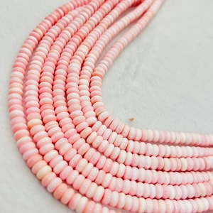 May include: A strand of pink coral beads, with a smooth, rounded shape. The beads are strung together on a clear thread.