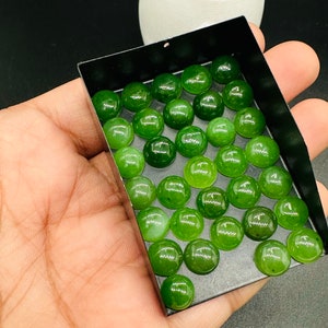 Könnte beinhalten: Eine Sammlung kleiner, runder, polierter grüner Edelsteine, wahrscheinlich Jade, präsentiert in einer schwarzen rechteckigen Schale. Die Steine haben eine glänzende Oberfläche und variieren leicht in der Farbgebung.