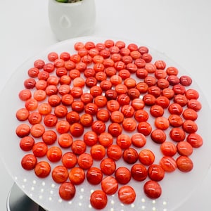 May include: A collection of approximately 50 round, red, and white cabochon gemstones. The gemstones are arranged in a circular pattern on a white surface.