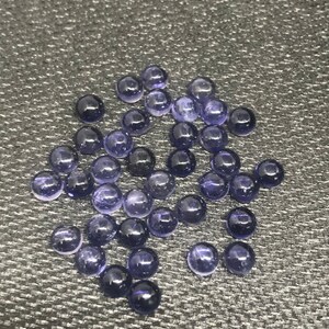 May include: A collection of round, purple gemstones, likely amethyst, displayed on a textured gray surface.