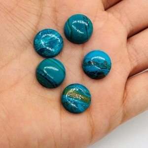 May include: Five round, polished gemstones in shades of teal and turquoise, with swirling patterns and natural variations. The stones are displayed on a hand, showcasing their color and texture. These stones could be used for jewelry making or other crafts.