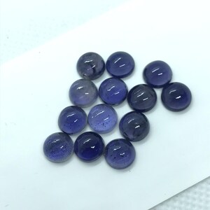 May include: A collection of 14 round, purple, gemstone cabochons. The cabochons are smooth and polished, with a slight shimmer.