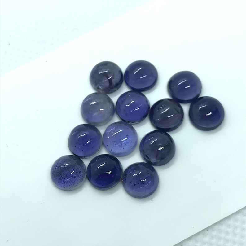 May include: A collection of 14 round, purple, gemstone cabochons. The cabochons are smooth and polished, with a slight shimmer.