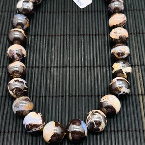 May include: A necklace made of brown and white opal beads. The beads are round and have a smooth, polished finish. The necklace is 18 inches long and has a 40 cm circumference. The necklace is on a black bamboo mat.