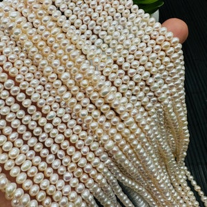 Op de afbeelding: Een streng witte zoetwaterparels, met een licht crèmekleurige tint, gerangschikt in een cascadepatroon. De parels zijn rond en glad, met een subtiele glans.