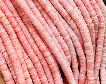 May include: A strand of pink and white shell beads. The beads are round and flat, and they are strung on a thin cord. The beads are approximately 1.2 cm in diameter.
