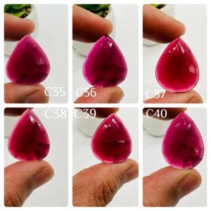 May include: Six faceted, teardrop-shaped gemstones in varying shades of deep pink to red are displayed. Each gem is held between fingers, with the labels C35, C36, C37, C38, C39, and C40 visible. The gems have a polished, reflective surface.