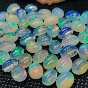 May include: A collection of oval-shaped, iridescent opal gemstones. The opals are a milky white color with flashes of blue, green, and red.