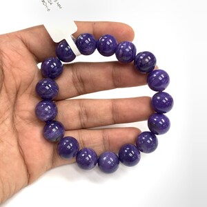 Puede incluir: Un brazalete hecho de grandes cuentas redondas y pulidas de color púrpura. Las cuentas están ensartadas para formar una forma circular. La etiqueta dice "12,5 mm" y "#CH-6".