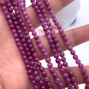 May include: A strand of pink gemstone beads, strung on a red thread. The beads are round and smooth, and they are arranged in a symmetrical pattern. The beads are approximately 4mm in diameter.