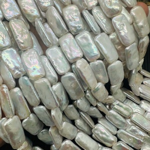 May include: A strand of white baroque freshwater pearls, each pearl is rectangular and has an iridescent sheen.